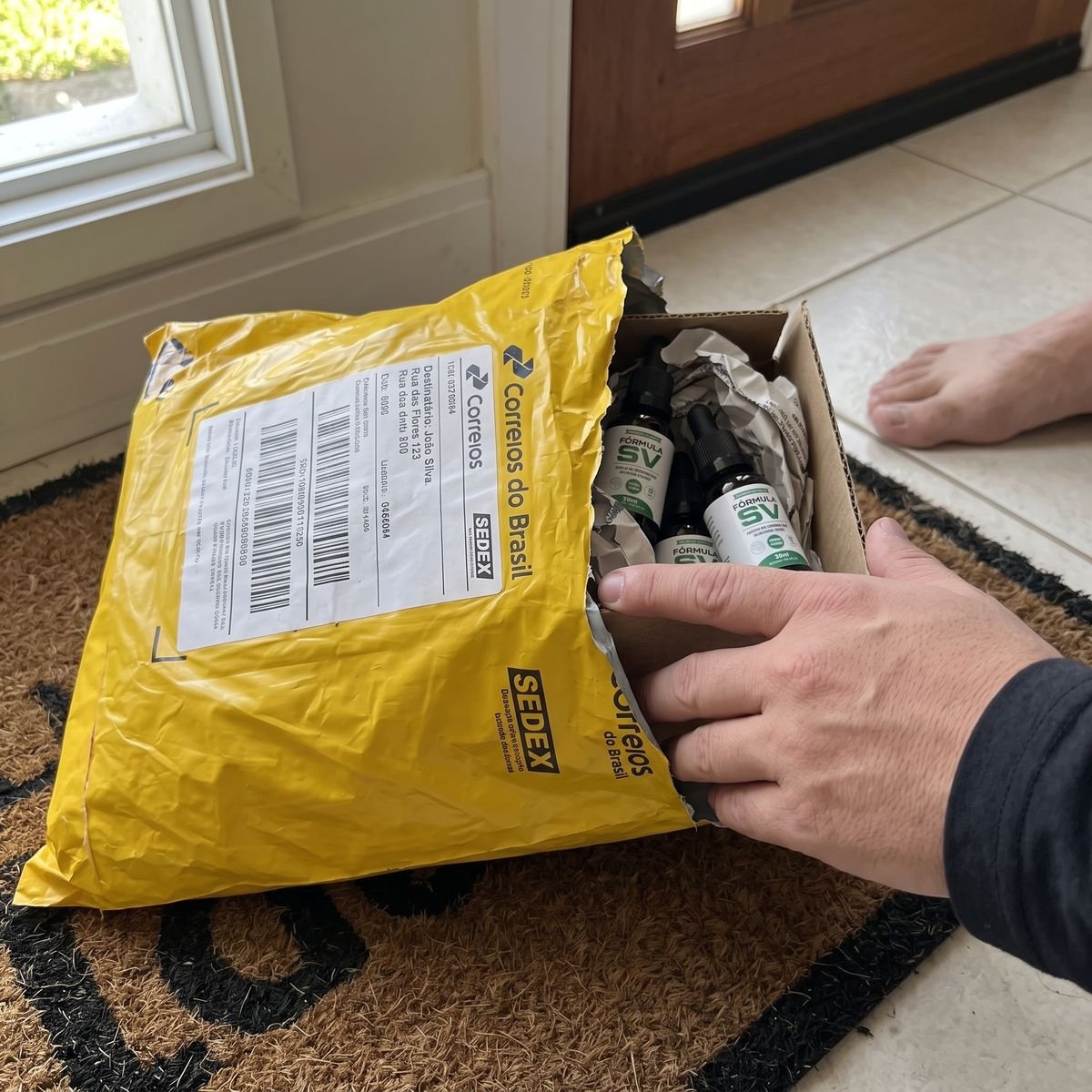 Encomenda dos Correios aberta na porta, com os frascos da Fórmula SV dentro da caixa.